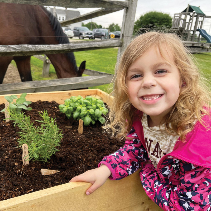 little girl smiling next to a flower bed